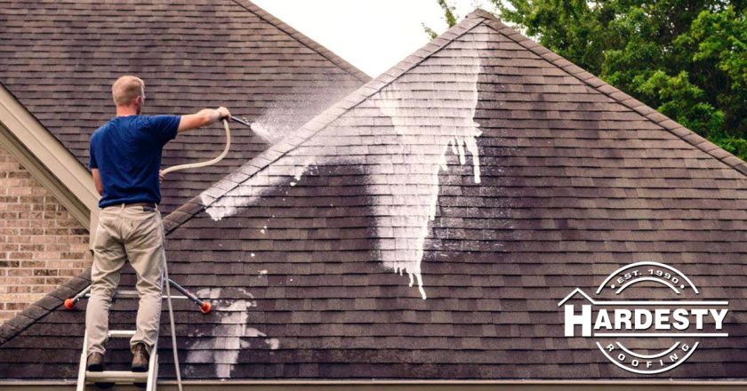 A Hardesty technician soft-washing a shingle roof from a ladder